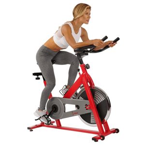 A woman exercises on a red stationary bike from Sunny Health & Fitness, wearing a white sports bra and gray leggings.