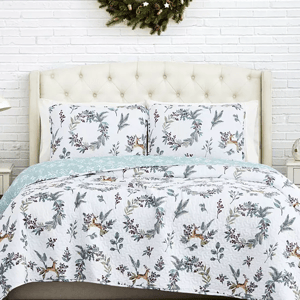 A queen-size quilt set featuring a winter motif with reindeer and holly, in a white and soft blue color scheme.