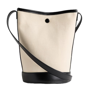 The Gap Factory Canvas Bucket Bag features a beige canvas body with a black leather base, trim, and strap. It includes a button closure at the top for security.