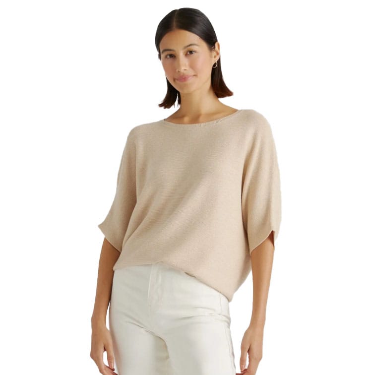 A woman is wearing a beige Cotton-Cashmere Dolman Sweater with loose-fitting sleeves and a relaxed fit, paired with white pants.