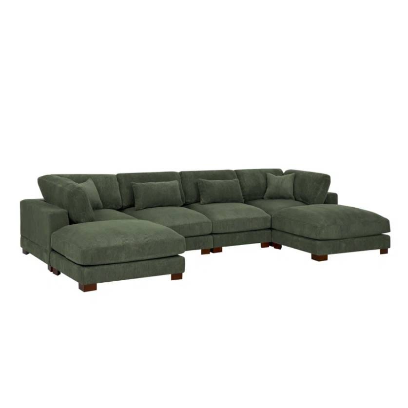 The Wade Logan Andreco Sofa is a large, L-shaped sectional sofa with plush cushions, upholstered in a deep green fabric. It features wide armrests and solid block legs, creating a modern and comfortable seating option.