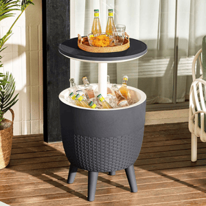A round, elevated side table with a wicker-style finish features a built-in cooler compartment filled with ice and bottles. The tabletop above holds a tray with drinks and snacks.
