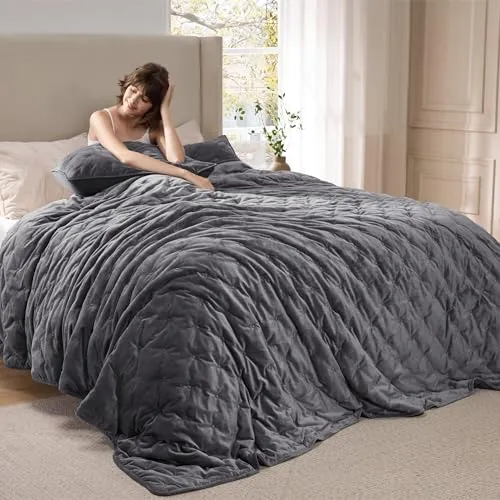 A gray velvet weighted blanket is draped over a bed with a person sitting up, holding a matching pillow.