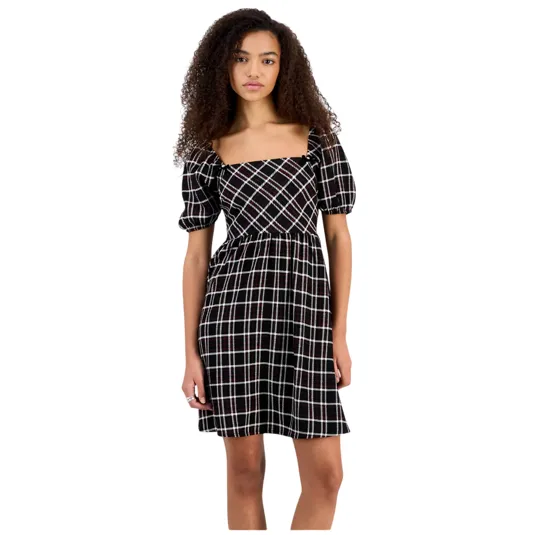A young woman wears a black and white checkered dress with puffed sleeves and a square neckline, standing against a plain background.