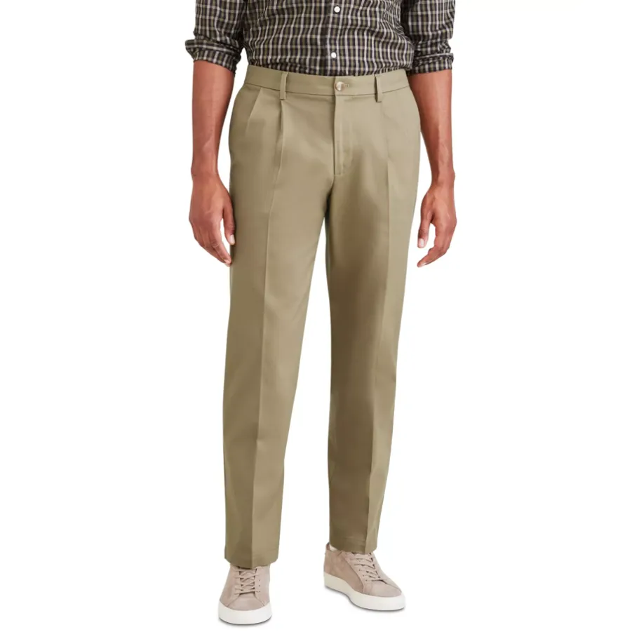 A person is wearing beige pleated dress pants paired with a plaid dress shirt and beige sneakers.