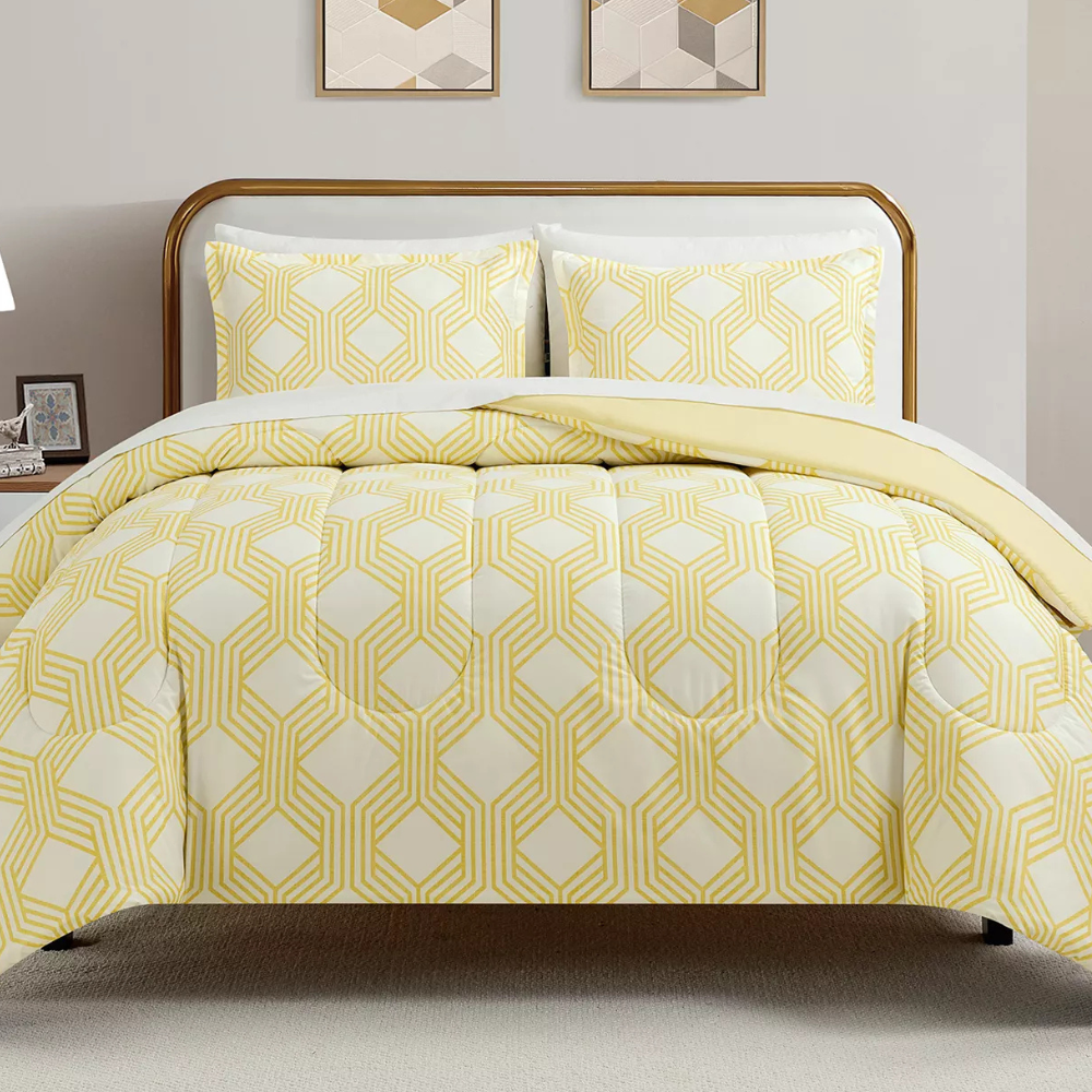 A bed features a comforter and pillowcases with a yellow geometric pattern on a white background. Two framed geometric prints hang on the wall above the bed.