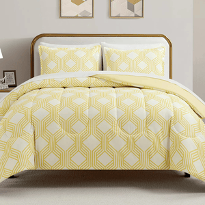A bed features a comforter and pillowcases with a yellow geometric pattern on a white background. Two framed geometric prints hang on the wall above the bed.