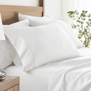 White bed with neatly arranged pillows and sheets, adorned with a wooden headboard and complemented by a potted plant nearby.