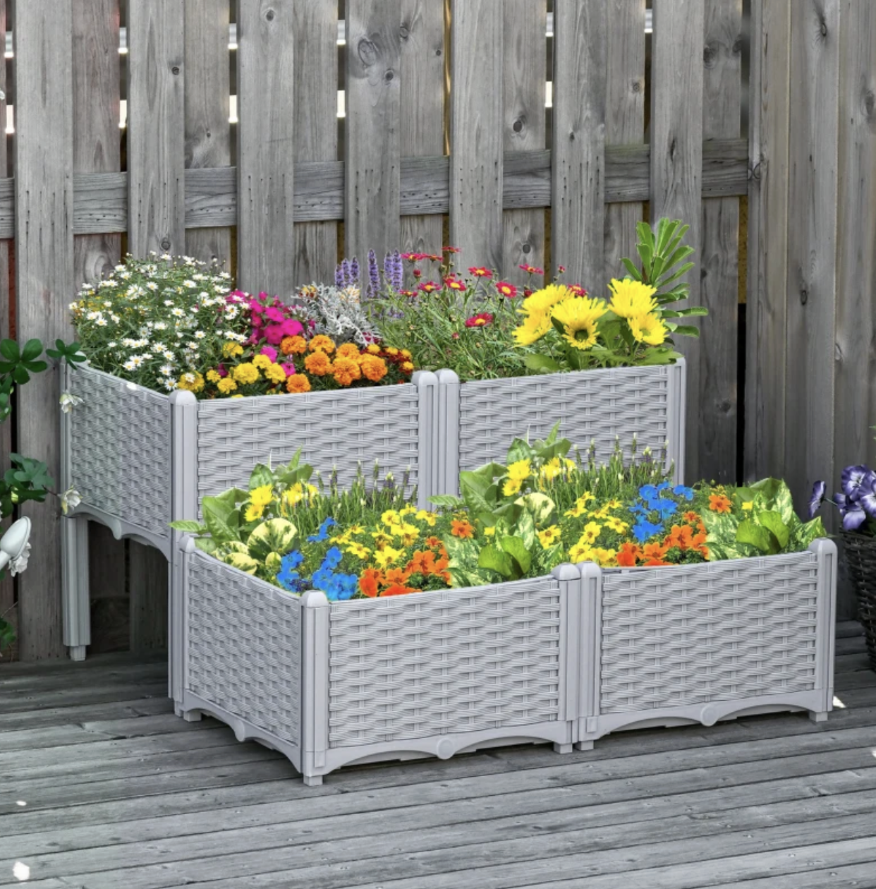 Two-tier grey wicker-style raised garden bed with a variety of colorful flowers against a wooden fence.