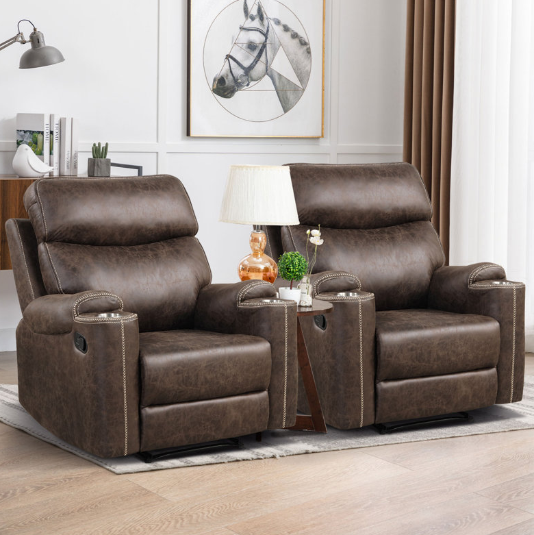 Two brown vegan-leather recliners with high backs and nailhead trim, featuring integrated cup holders and manual recline levers, set on a light wood floor beside a triangular side table with a lamp.