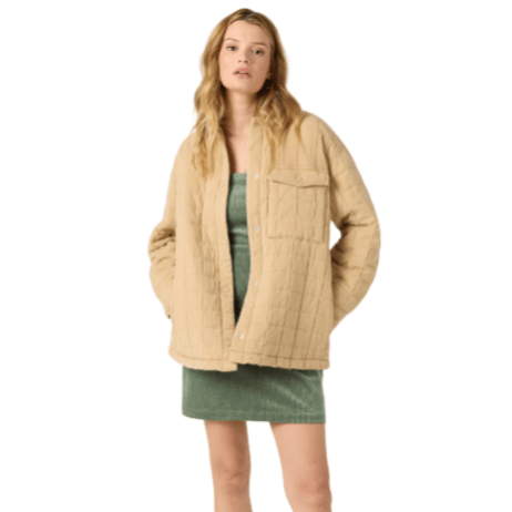 A model wearing a green sleeveless dress with a textured fabric and an oversized beige quilted jacket featuring a chest pocket and snap buttons.