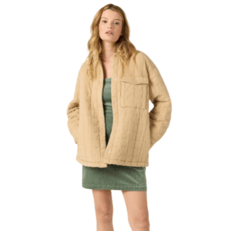 A model wearing a green sleeveless dress with a textured fabric and an oversized beige quilted jacket featuring a chest pocket and snap buttons.