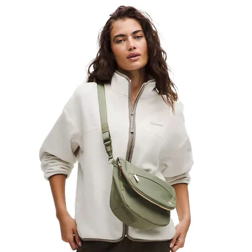 A woman is wearing a zip-up jacket and carrying a light green crossbody bag.