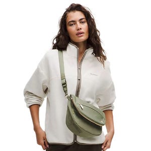 A woman is wearing a zip-up jacket and carrying a light green crossbody bag.