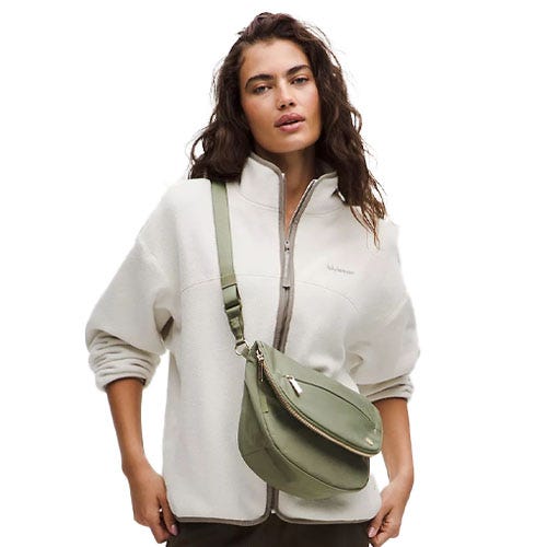 A woman is wearing a zip-up jacket and carrying a light green crossbody bag.