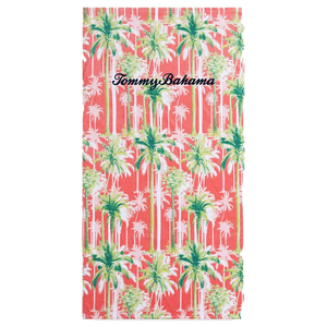 A beach towel with a tropical palm tree print and \“Tommy Bahama\“ embroidered on it. The background color is coral.