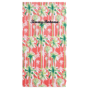 A beach towel with a tropical palm tree print and \“Tommy Bahama\“ embroidered on it. The background color is coral.