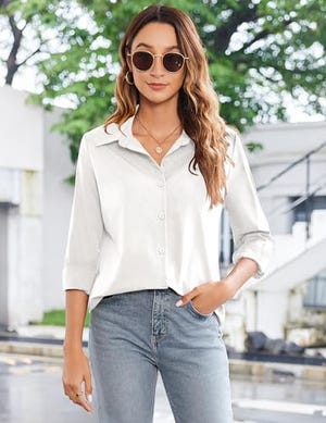 A woman wearing a relaxed-fit, white button-down shirt with rolled-up sleeves, paired with blue jeans and sunglasses.