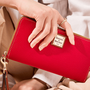 A vibrant red Dooney & Bourke Large Zip-Around Wallet features a textured leather design, gold-tone hardware, and a logo plate on the front. The wallet includes a detachable wrist strap for convenience.