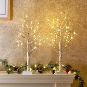 Lighted birch tree decorations with warm white lights are placed on a mantel alongside green pine garland and pine cones.