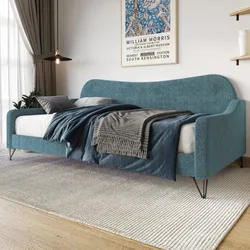 A blue upholstered daybed with metal legs is adorned with gray and navy bedding. Nearby are a curtain, a plant, and a framed William Morris poster on the wall.