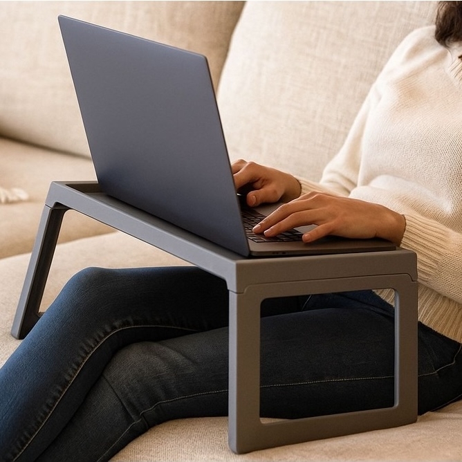 A person is using a laptop on a portable lap desk with foldable legs while sitting on a couch.