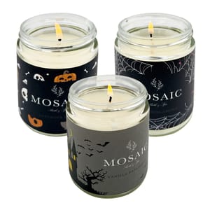 Three lit Halloween-themed scented candles with black labels featuring bats, spiders, and pumpkins designs.