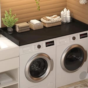 A laundry setup featuring a front-loading washing machine and dryer beneath a black countertop, with towels, a plant, and toiletries neatly arranged on top.