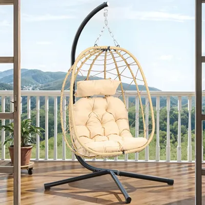 A hanging egg chair with a beige cushion is set on a balcony, featuring a metal stand and a woven basket design.
