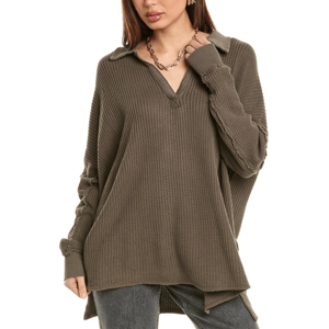 The Free People Travis Polo Shirt is an oversized, long-sleeve waffle knit in an olive green color with a V-neck and collar. It features a relaxed fit and raw edge details, paired with a chain necklace.