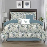 A floral-patterned comforter set on a bed, featuring teal and white flowers with matching pillows. The room includes two side tables with lamps and framed art above the headboard.