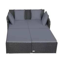 Rattan daybed with gray cushions and four pillows, designed for outdoor use. Suitable for lounging, its structure features a woven pattern and a sturdy frame.