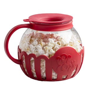 A glass microwave popcorn popper with a red silicone top and handle, featuring a red protective silicone band around the base. The band has \“Pop Corn\“ embossed on it.