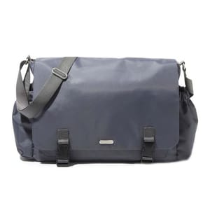 A dark gray Baggallini messenger bag with a large flap, adjustable shoulder strap, and two front buckles. It has elastic side pockets and a small metal logo plate on the front.