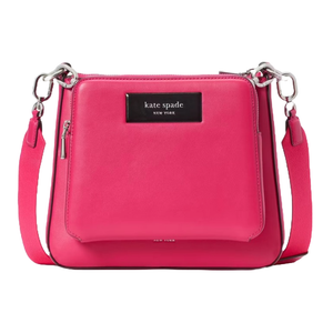 A pink Kate Spade New York crossbody bag with a black logo plate, silver hardware, and an adjustable strap.
