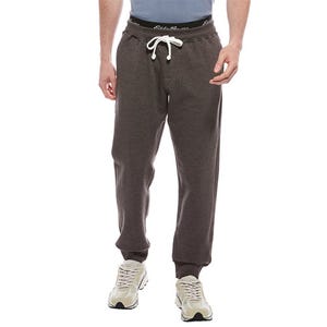 A person wearing dark gray jogger pants with a white drawstring and white sneakers, featuring a black waistband with white text.