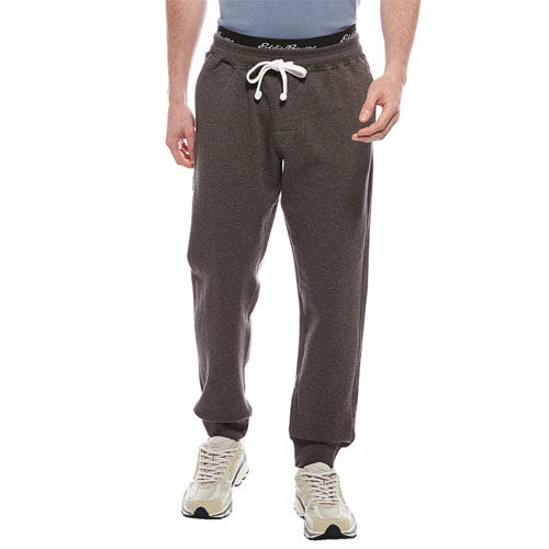 A person wearing dark gray jogger pants with a white drawstring and white sneakers, featuring a black waistband with white text.