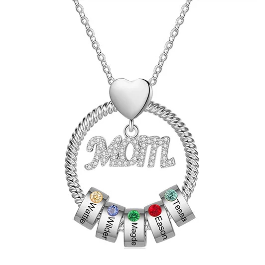 A necklace with a heart-shaped pendant holding a circular ring. Inside the ring is the word \“MOM\“ in ornate letters, accompanied by rings with colored gemstones and engraved names: Mattie, Wilder, Maggie, Eason, Tessa.