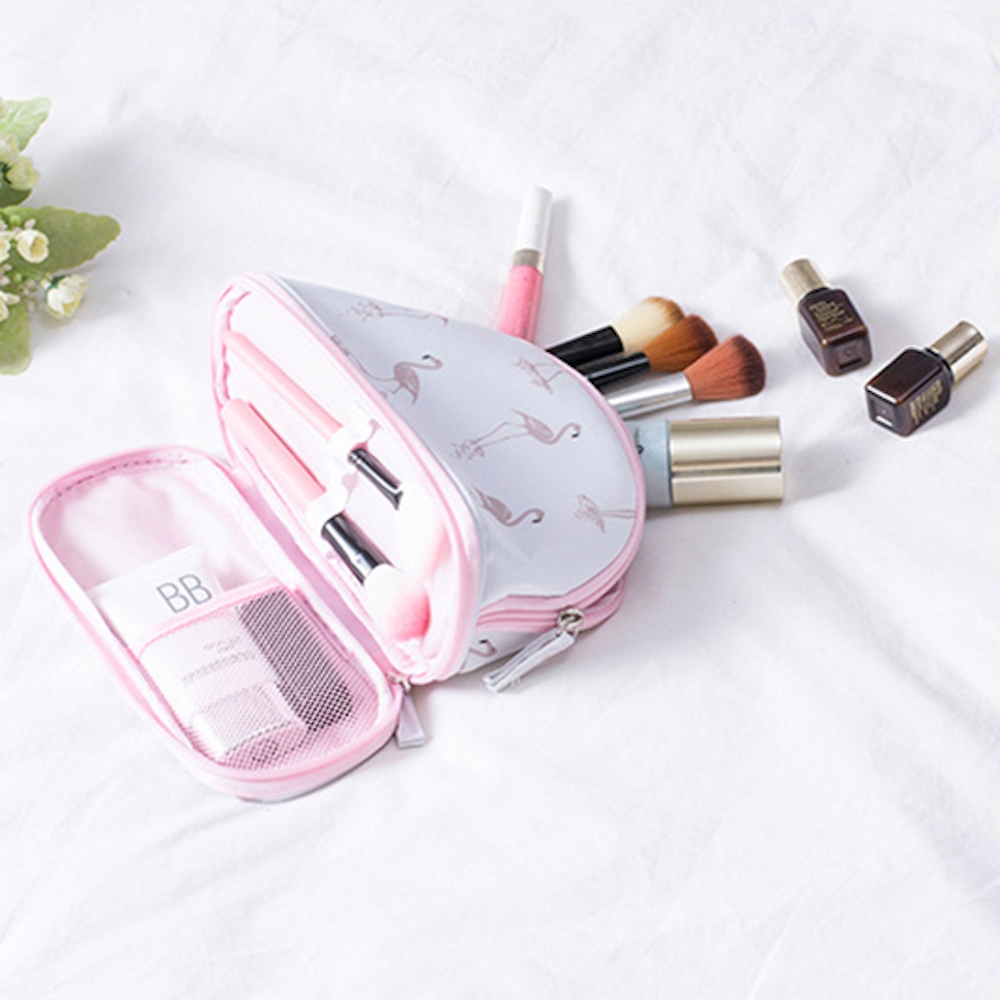 A pink flamingo-patterned makeup bag with various cosmetics and makeup brushes spread out beside it.