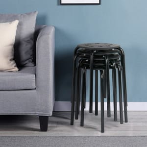 A set of five black stackable stools with round seats and metal legs, neatly nested together, placed beside a gray sofa in a room with a blue wall.