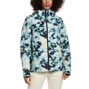 A person wearing a tie-dye patterned jacket with a high collar, hood, and multiple pockets, paired with light-colored pants.