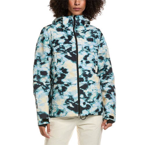 A person wearing a tie-dye patterned jacket with a high collar, hood, and multiple pockets, paired with light-colored pants.