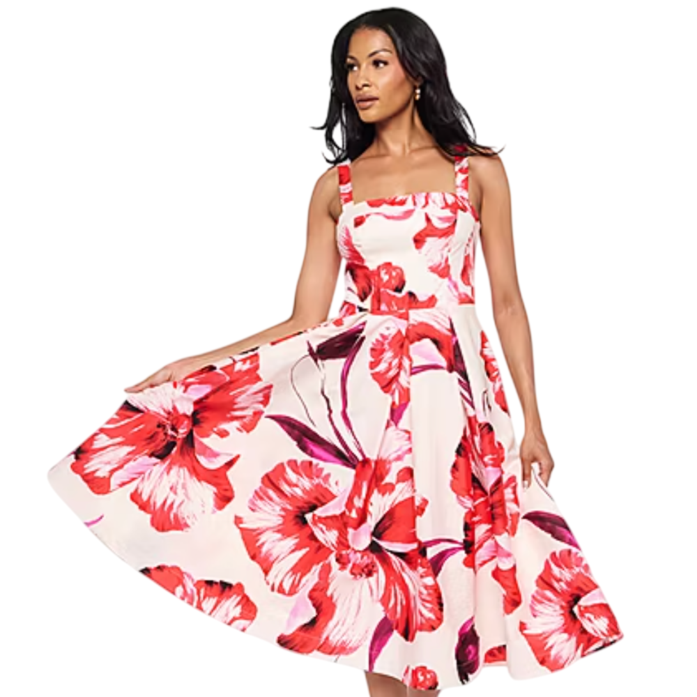 A woman wears a sleeveless dress with a red and pink floral print on a light background, featuring a fitted bodice and a flared skirt.