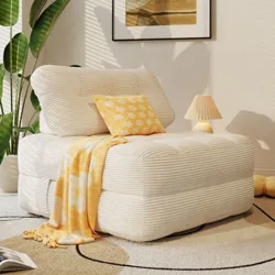 A cozy beige armchair with ribbed upholstery is styled with a yellow floral pillow and matching throw. There's a small lamp, a potted plant, and an open book nearby, set against a neutral rug and wall art.