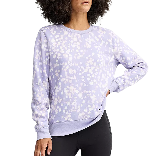 A person wears a lavender sweatshirt with a white speckled pattern, paired with black leggings.
