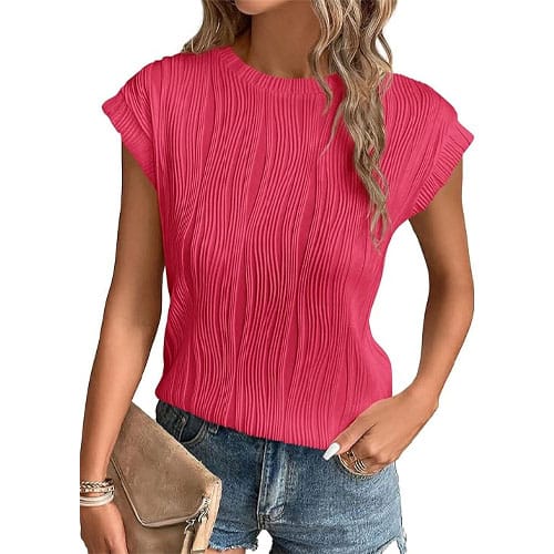 A woman wears a textured pink short-sleeve top paired with denim shorts and holds a tan clutch.
