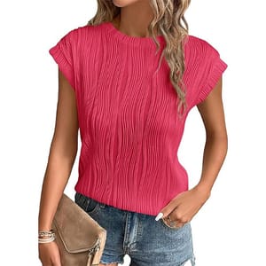 A woman wears a textured pink short-sleeve top paired with denim shorts and holds a tan clutch.
