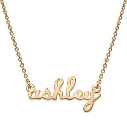 A gold necklace features a pendant with the name \“ashley\“ written in cursive.