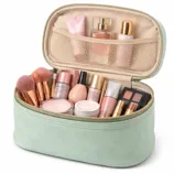 A mint green cosmetic bag is open, revealing makeup essentials like brushes, foundation, blush, eyeshadow palette, lipstick, and skincare products. The interior pocket holds bottles and tubes, neatly organized.