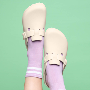 Feet in lavender socks with white and light purple stripes, wearing beige slip-on sandals against a mint green background.
